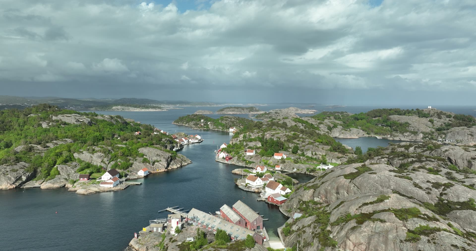 Industrial waterfront structure dominates foreground cove, Ny-Hellesund, Norway