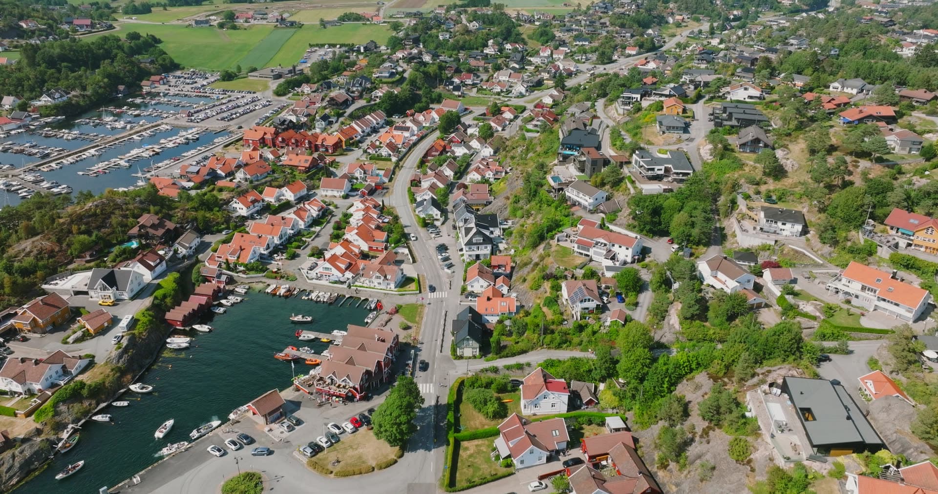 Hillside residential sprawl above working harbor basin, Høllen, Norway