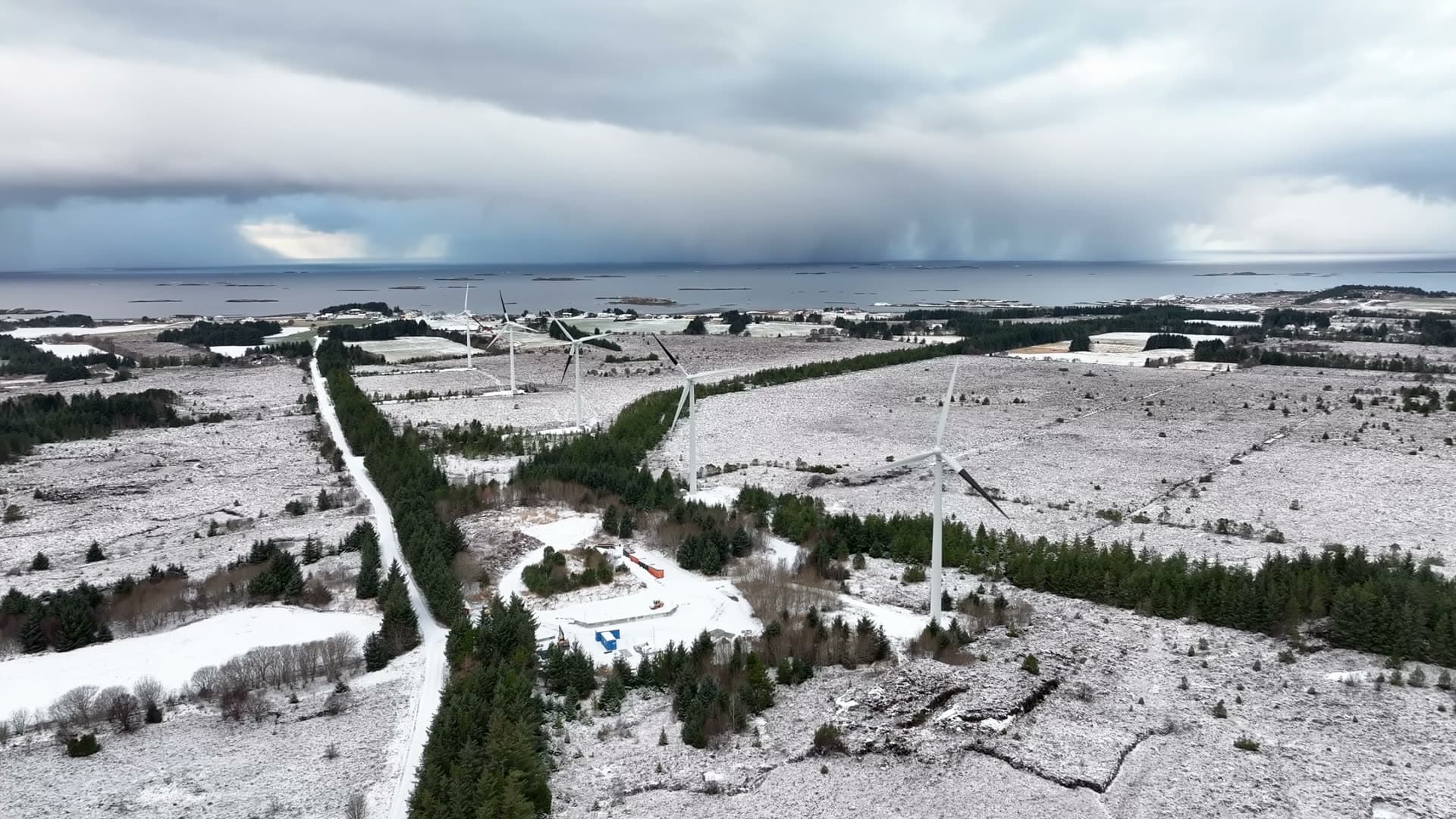 Wind farm and access roads across snowy coastal woodland, Harøy