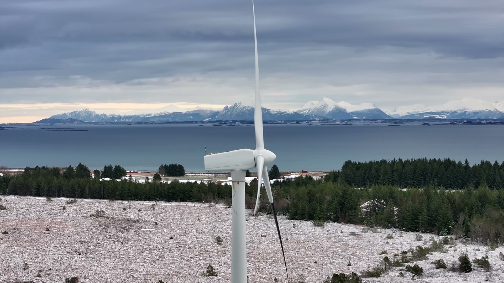 Wind turbine in profile against the sea and snowy mountains, Harøy