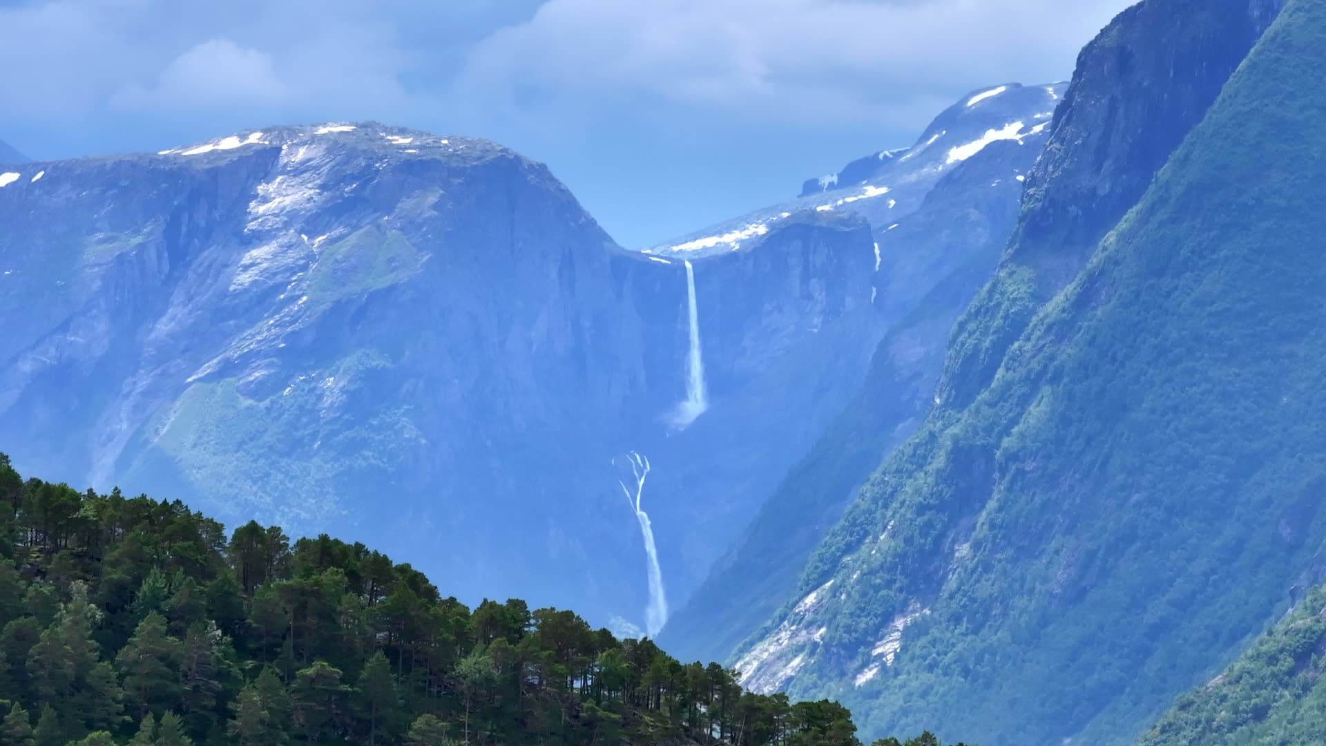 Mardalsfossen waterfall emerging above a wooded ridge in Eikesdal