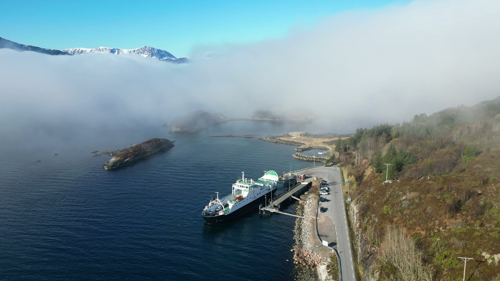 Car ferry departing Dryna beneath low fog and snowy mountains