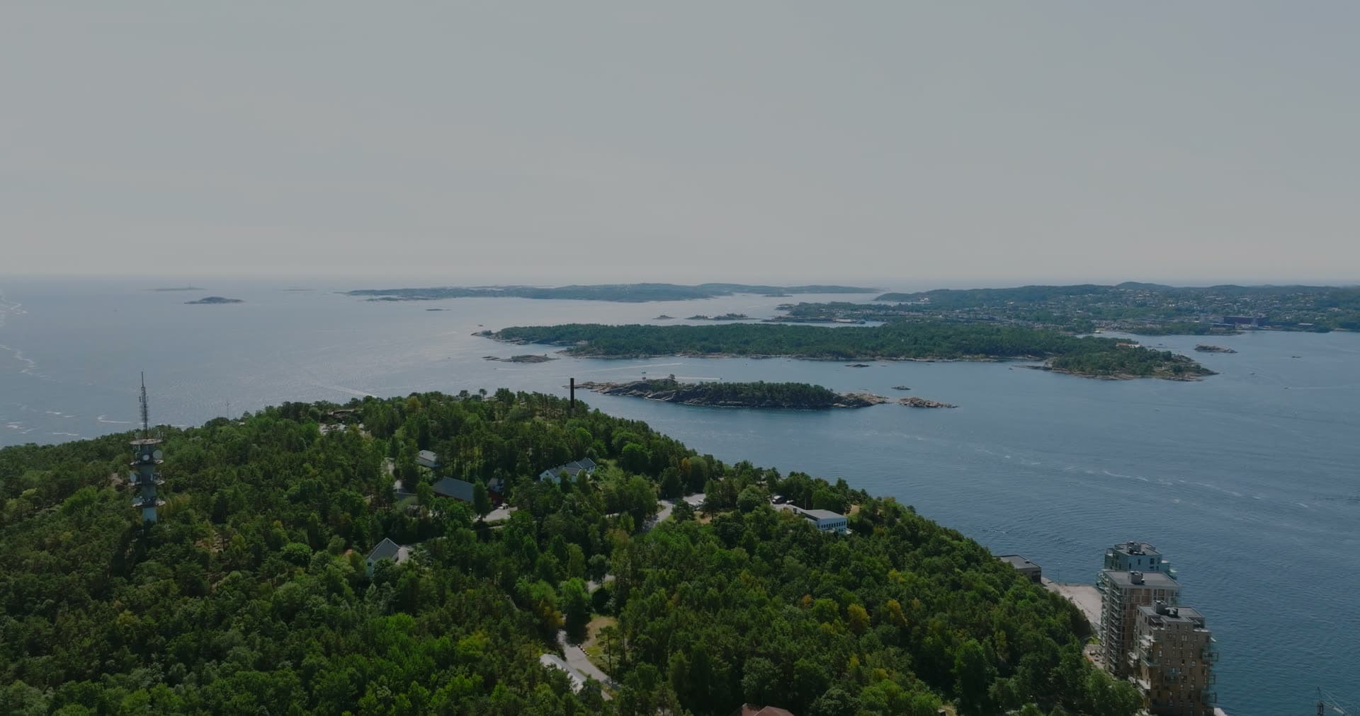 Dense conifer forest with scattered buildings and archipelago beyond, Kristiansand, Norway