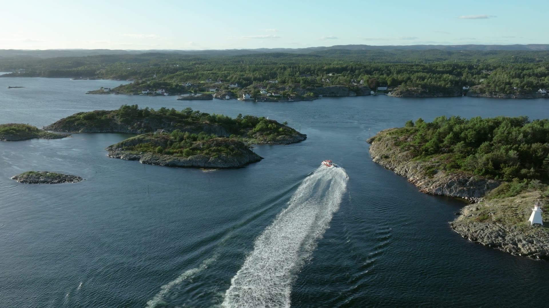 Speedboat wake curving between rocky forested islands, Lillesand, Norway