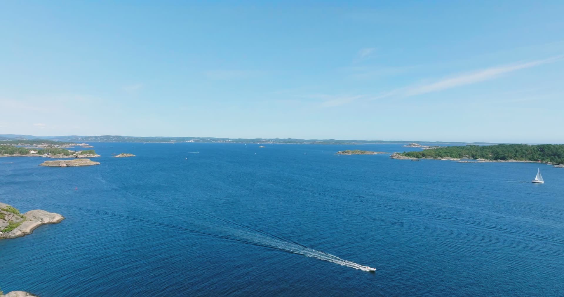 Speedboat towing wake across open blue archipelago, Skålevik, Norway