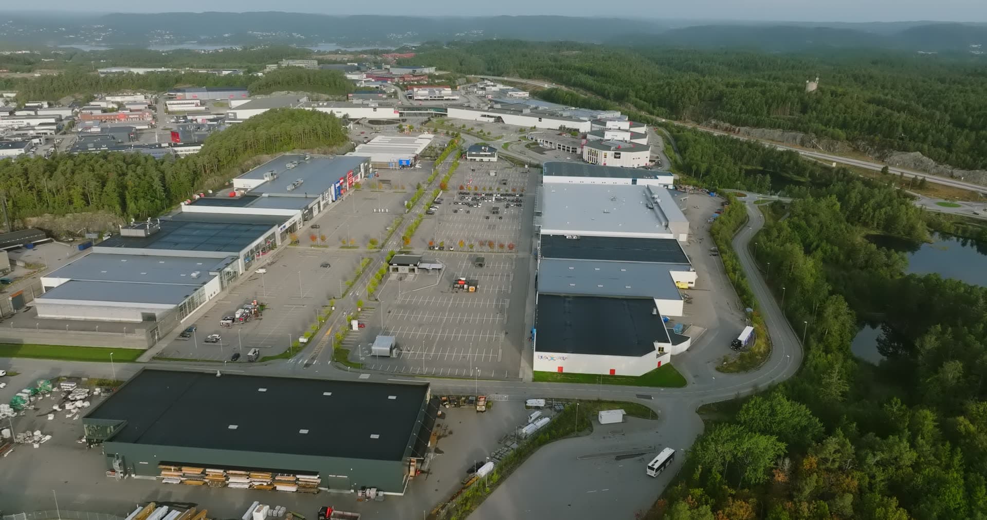 Retail complex with rain-soaked pavement and forest perimeter, Sørlandsparken, Kristiansand, Norway