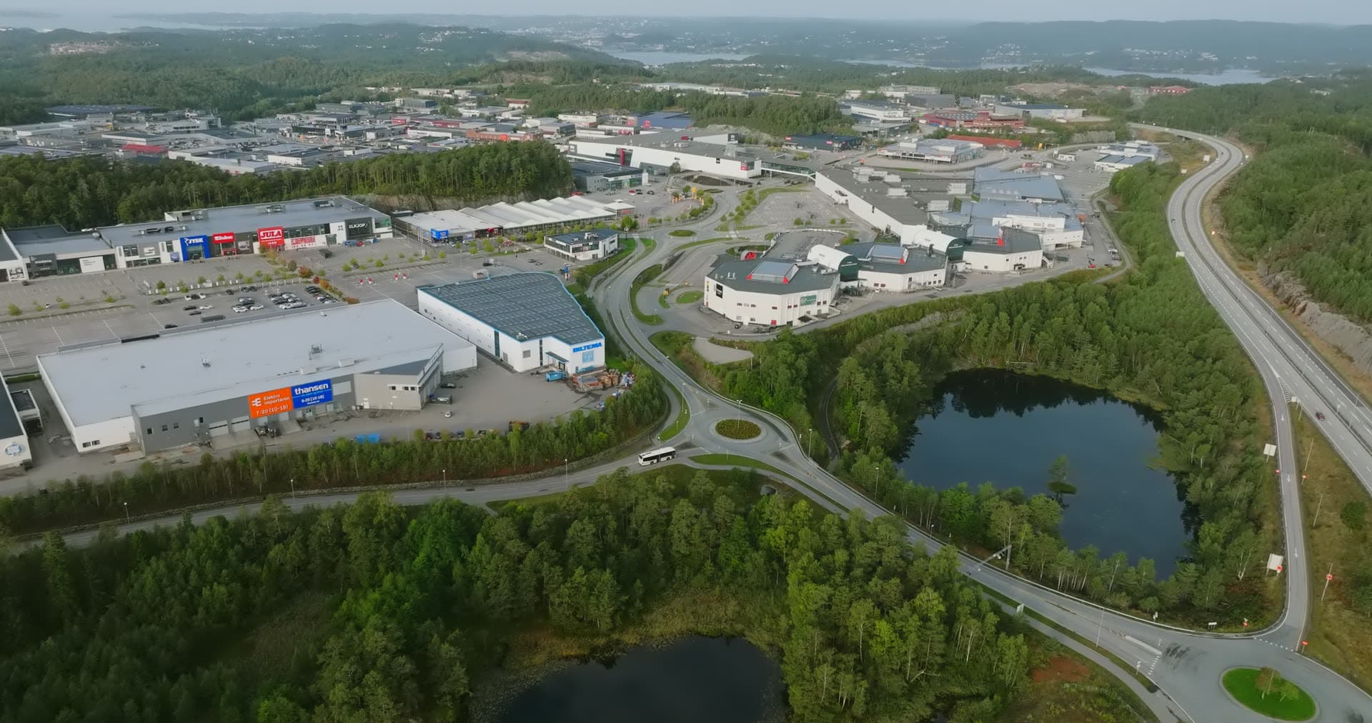 Curved access road connecting warehouse complexes through forest, Sørlandsparken, Kristiansand, Norway