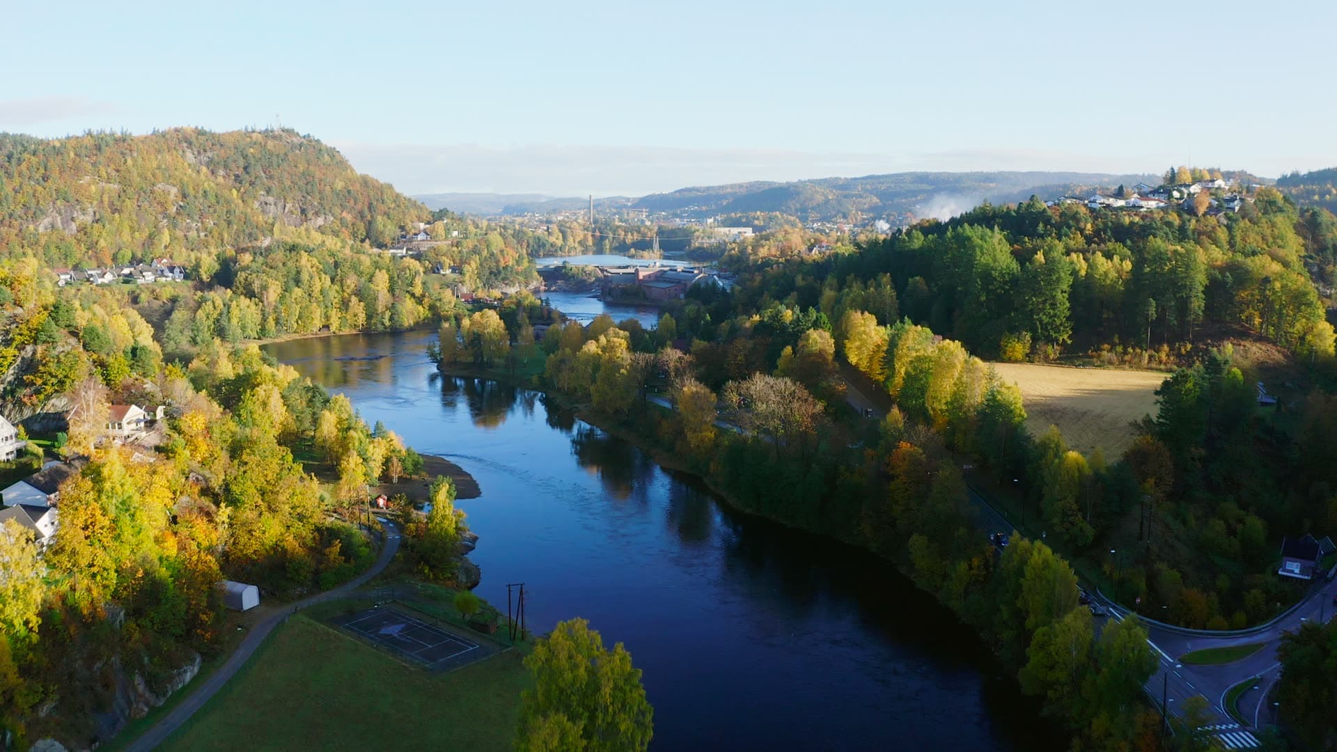 River bend through forested valley with distant city, Vigeland, Vennesla, Norway